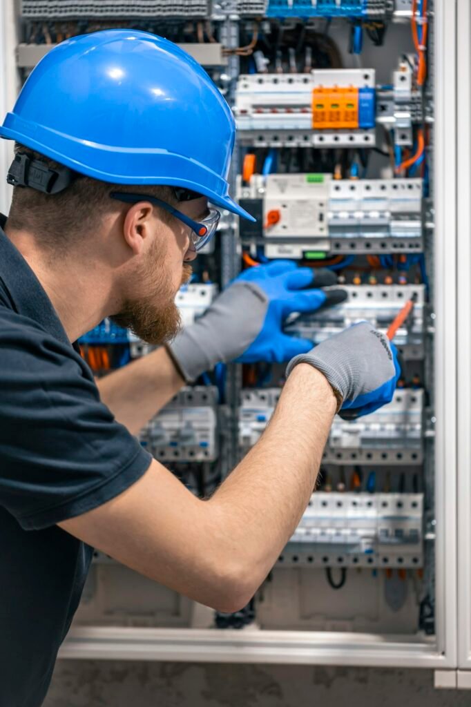 A male electrician works in a switchboard with an electrical connecting cable.